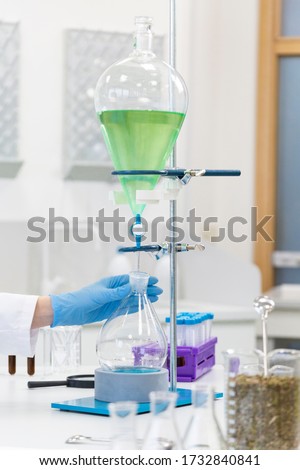 Close up shot of hand wearing rubber gloves work with blue liquid in separatory funnel that is place. Laboratory environment.