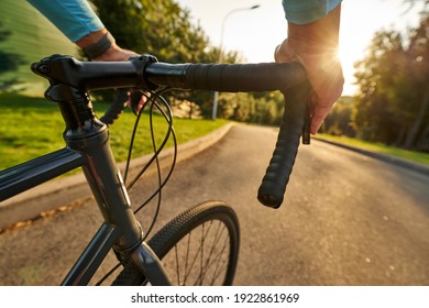 Close up shot of hands on handlebar. Professional male bicycle racer riding his road bike in the park at sunset