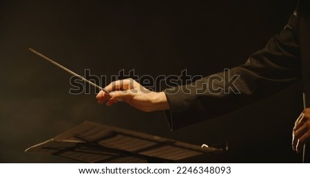 Close up shot of hands of symphony orchestra conductor directing music by waving his baton. Studio shot on black background 