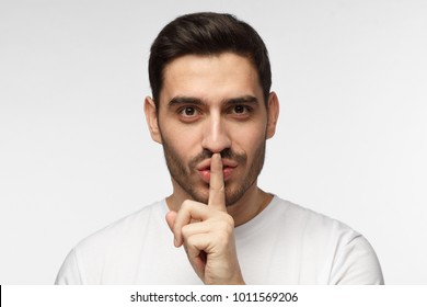 Close up shot of handsome tricky man with shh gesture, asking for silence or to be quiet, isolated on gray background - Powered by Shutterstock