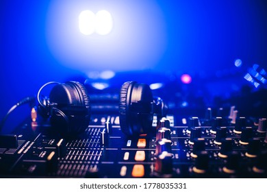 Close Up Shot Headphones On DJ Mixing Board In Night Club With Blue Light. Black Mixing Sound Console For Good Sound Close Up.