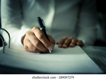 Close shot of a human hand writing something on the paper on the foreground