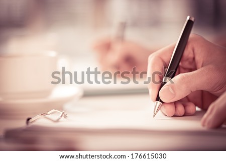 Close shot of a human hand writing something on the paper on the foreground  Foto d'archivio © 