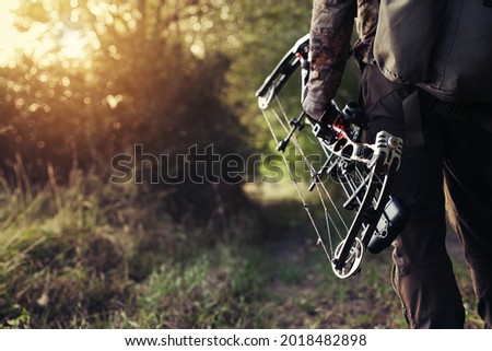 Close up shot of a hunter dressed in camouflage clothing holding a modern bow.