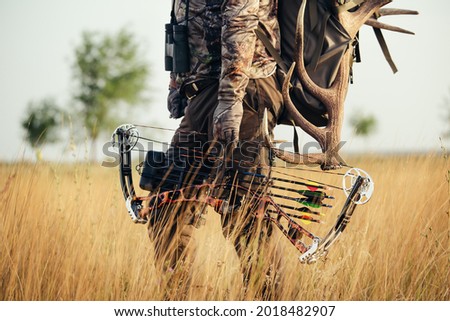 Close up shot of a hunter dressed in camouflage clothing holding a modern bow.
