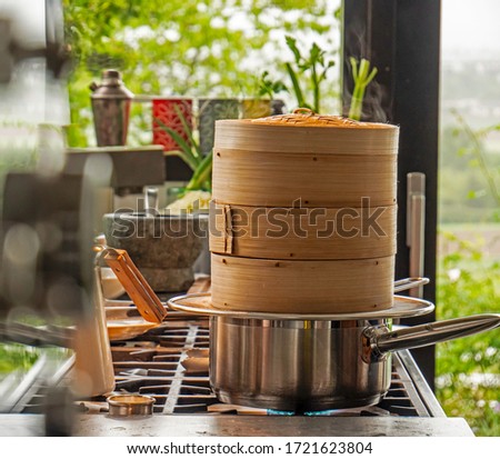Close up shot of a Japanese cooking Steamer. The steamer stands on top of boiling water cooking food in a rustic beautiful kitchen. Steam can be seen coming form the top of the steamer.