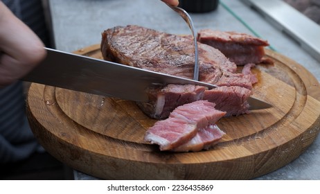 Close up shot of a juicy freshly grilled steak straight from the grill being cut with fork and knife on kitchen table