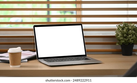 Close up shot of laptop with white screen, paper cup of coffee and houseplant on wooden table - Powered by Shutterstock