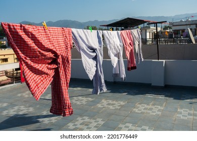 A close up shot of laundry drying outside under sun. Shirts hanging on a wire on the roof. Dehradun City, Uttarakhand India.
