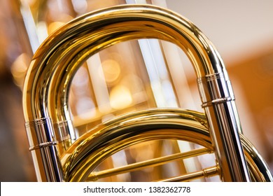 A close up shot of the main tuning slide of a Professional Bass Trombone with a line of trombones in the background out of focus with a bokeh background. Very warm tones of brass. - Powered by Shutterstock