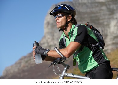 Close up shot of a male cyclist holding a water bottle with a mountain in the background.