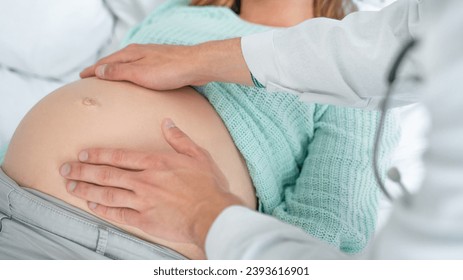 Close up shot of male doctor examining pregnant woman lying on bed in clinic. Palpation of womb belly, feeling baby fetus embryo bumps. Gynecologist checkup - Powered by Shutterstock