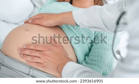 Close up shot of male doctor examining pregnant woman lying on bed in clinic. Palpation of womb belly, feeling baby fetus embryo bumps. Gynecologist checkup