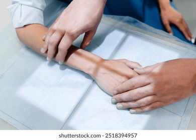 Close up shot of a male doctor places the hand of a female patient to take an x-ray on a special stand in an office with an x-ray machine, medical equipment. Woman having x-ray shot of broken hand - Powered by Shutterstock