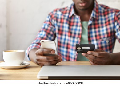 Close Up Shot Of Male Hands Holos Mug Debit Cad And Mobile Phone, Entering Data For Web-site Form, Going To Pay For Online Order. People, Lifestyle, Modern Technologies And E-commerce Concept