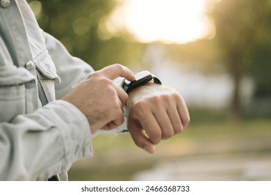 Close up shot of male's hand uses of wearable smart watch at outdoor in sunset. Man's hand touching a smartwatch. Smart watch. Smart watch on a man's hand outdoor.