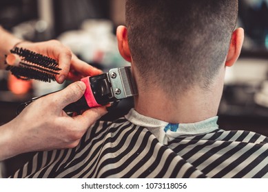 Close up shot of man getting trendy haircut at barber shop. Male hairstylist serving client, making haircut using machine and comb.
