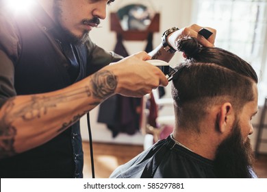 Close up shot of man getting trendy haircut at barber shop. Male hairstylist serving client, making haircut using machine and comb. - Powered by Shutterstock