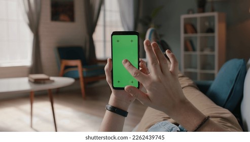 Close up shot of man lying on couch and using smart phone with chroma key green screen, doing various taps, swipes and scrolls - technology, communication  - Powered by Shutterstock