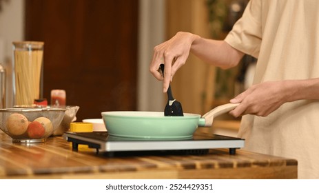 Close up shot of man stirring ingredients in frying pan with wooden spatula - Powered by Shutterstock