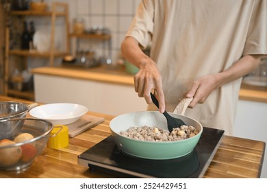 Close up shot of man stirring ingredients in frying pan with wooden spatula - Powered by Shutterstock