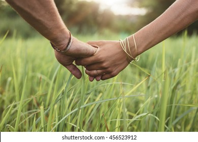 Close Up Shot Of Man And Woman Holding Hands In Grass Field. Young Couple In Love With Hand In Hand.