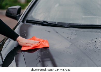 Close Up Shot Of Mans Hand Polishing Wet Car Hood With Microfiber Cloth. Unrecongizable Man Takes Care Of His New Black Auto.