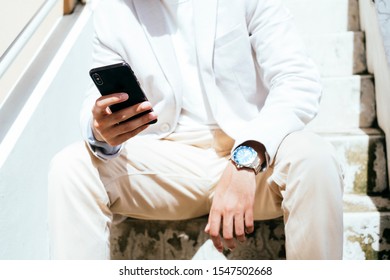 Close up shot of mobile in right hand and watch on left wrist of a man who sitting at the stair.