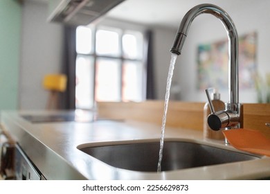 Close up shot of modern kitchen faucet with water running from tap, flow falling to empty dish sink at stylish home interior, selective focus, sustainable resources consumption concept - Shutterstock ID 2256629873