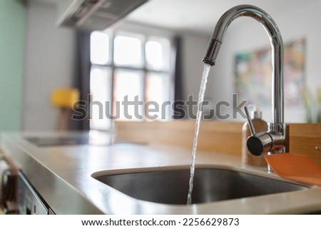 Close up shot of modern kitchen faucet with water running from tap, flow falling to empty dish sink at stylish home interior, selective focus, sustainable resources consumption concept