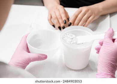 Close up shot of a nail technician mixing an alginate mask for hands, beautiful manicured nails in the background. - Powered by Shutterstock