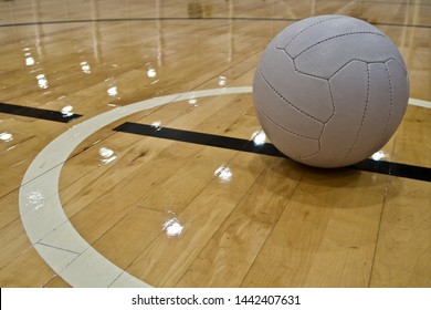 A Close Up Shot Of A Netball Ball Positioned Right Of Shot, Placed Within The Centre Circle On A Wooden Floor Board Indoor Netball Court.