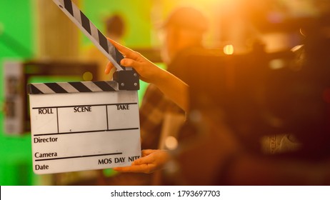 Close Up Shot On Film Studio Set Young Camera Assistant Holds Empty Clapperboard. In The Background Director Shooting Green Screen Scene. History Costume Drama Movie.