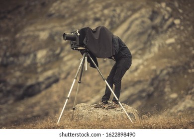 Close up shot of a photographer using a vintage camera on a tripod, backed by a mountain.