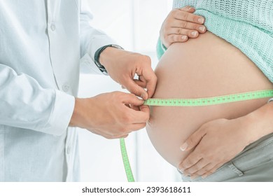 Close up shot of a pregnant woman exposing her belly while doctor uses a measuring tape to follow the growth of the baby at a hospital, indoors. - Powered by Shutterstock