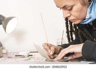 Close Up Shot Of Pretty Young White Girl Hispanic Latina Art Director With Frowning Brow Very Concentrated Tracing A Design In Onion Paper On Styrofoam, On Her Work Table Illuminated By A Lamp.