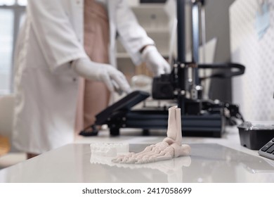 Close up shot of produced white-colored 3D dental and bone samples on acrylic print bed in laboratory, unrecognizable technician working in blurred background