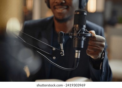 Close up shot of professional condenser microphone and African American male hand setting it up during live podcast in studio