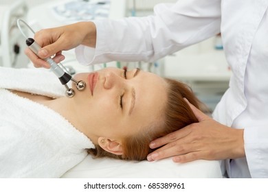 Close Up Shot Of A Professional Cosmetologist Performing Stimulating Facial Treatment For Her Female Client. Beautiful Woman Getting Microcurrent Facials At Spa Salon Skincare Electrodes Apparatus