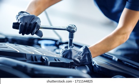 Close Up Shot Of A Professional Mechanic Working On Vehicle In Car Service. Engine Specialist Fixing Motor. Repairman Is Wearing Gloves And Using A Ratchet. Modern Clean Workshop.