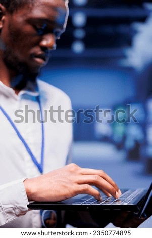 Close up shot of proficient computer scientist maintenancing server rows delivering web content to online clients. African american supervisor using laptop to ensure critical systems functionality