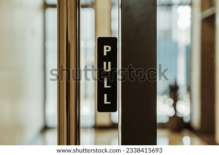 Close up shot of pull sign on glass door hotel lobby with stainless steel door handle. Bokeh background.