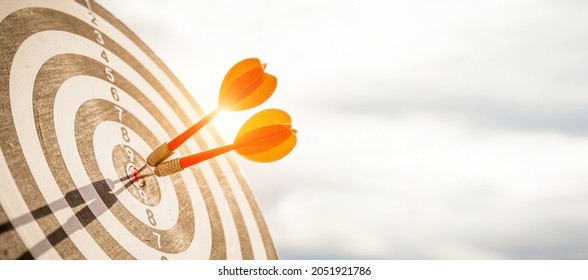 Close up shot red darts arrows in the target  of dartboard center on dark blue sky background. Business target or goal success and winner concept. - Shutterstock ID 2051921786