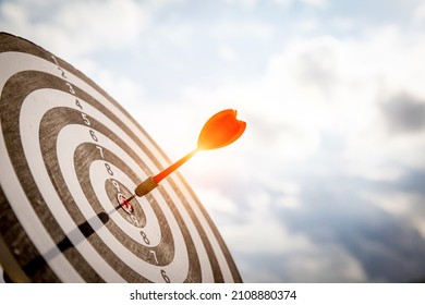 Close up shot red darts arrows in the target  of dartboard center on dark blue sky background. Business target or goal success and winner concept. - Shutterstock ID 2108880374