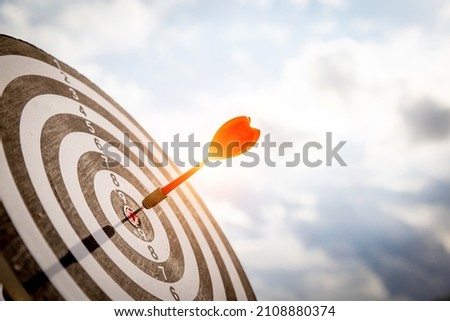 Close up shot red darts arrows in the target  of dartboard center on dark blue sky background. Business target or goal success and winner concept.