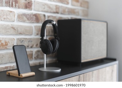 Close Up Shot Of Retro Style System, Stereo Speaker Or Column On Shelf With Mockup Display On Smartphone And Wireless Black Headphones Against Brick Wall At Home. Modern Acoustic Technology