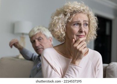 Close up shot of sad disappointed unhappy older woman suffers from misunderstanding or resentment sit on sofa with frown angry husband after quarrel. Break up, divorce, emotional abuse, bad relations