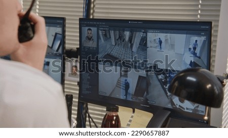 Close up shot of security officer controlling CCTV cameras, using walkie talkie and computers screens showing surveillance cameras footage with modern face scanning system. Concept of social safety.