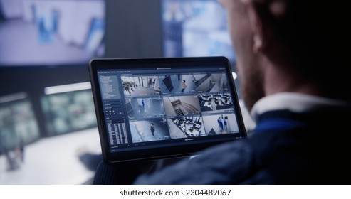 Close up shot of security officer zooming CCTV cameras with AI facial scanning using tablet in police surveillance center. Colleagues work at background. Monitoring system. Concept of social safety. - Powered by Shutterstock