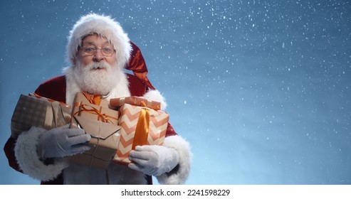 Close up shot of senior bearded man in santa clause outfit carrying gift boxes, isolated on blue background - christmas spirit, holiday mood . copy space - Powered by Shutterstock